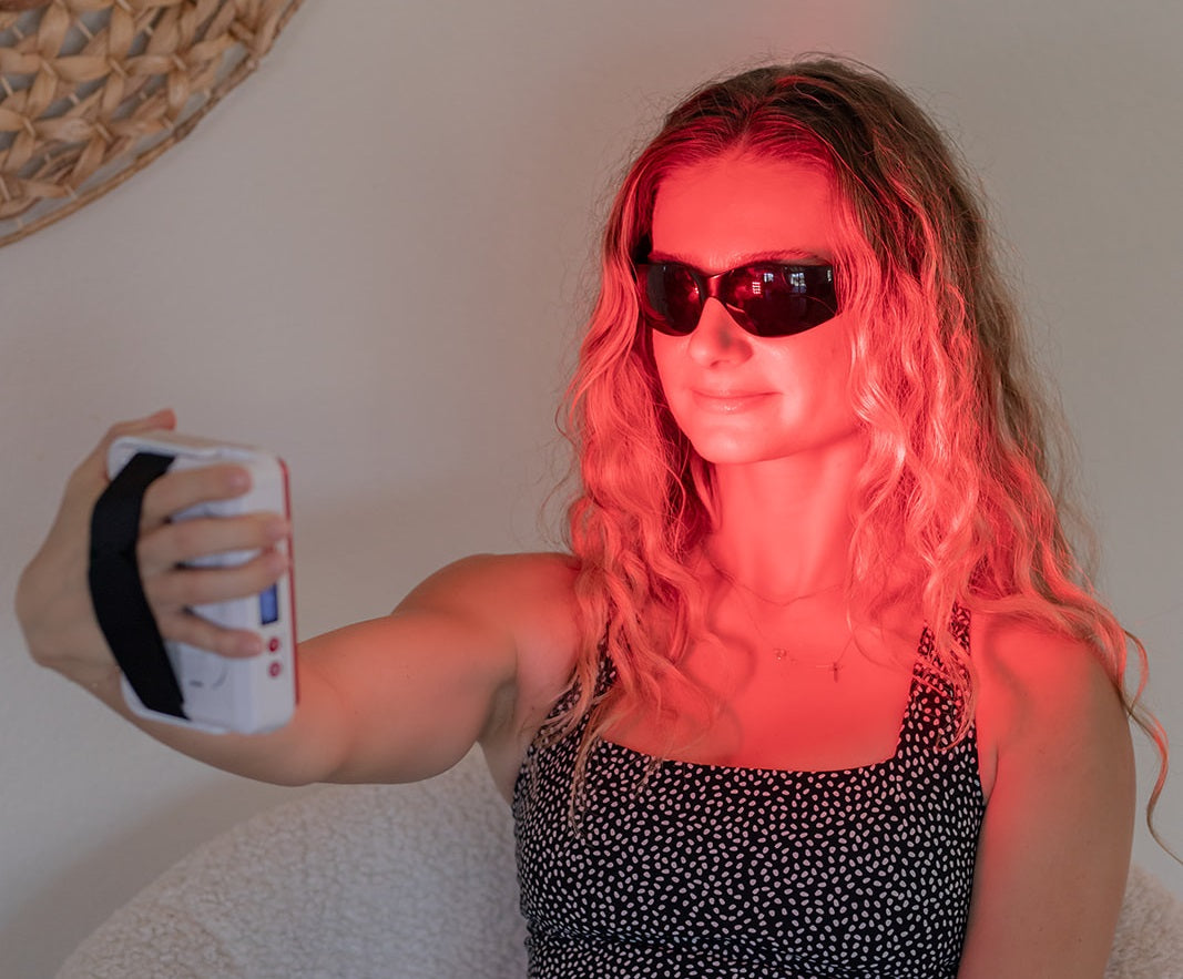 blonde woman using small mobile red light therapy panel at home.