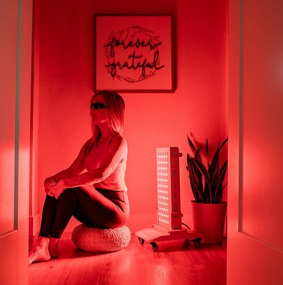 woman sitting in front of red light panel for session.