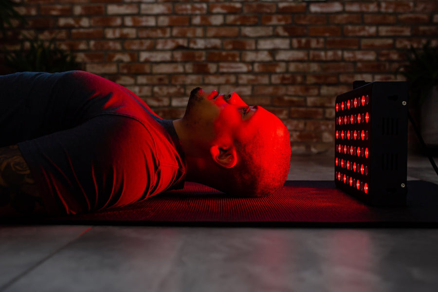 man laying down with red light therapy panel at this head to help with brain health.