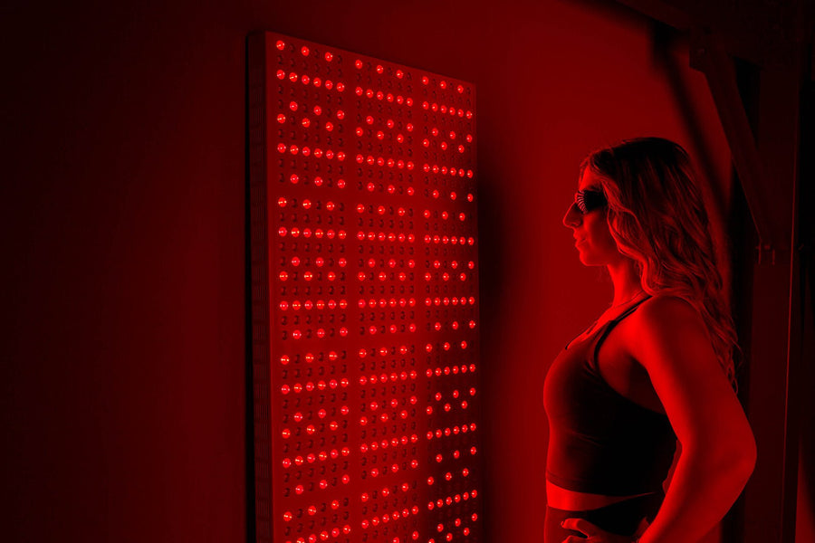 Woman in front of red light panel for near infrared therapy.