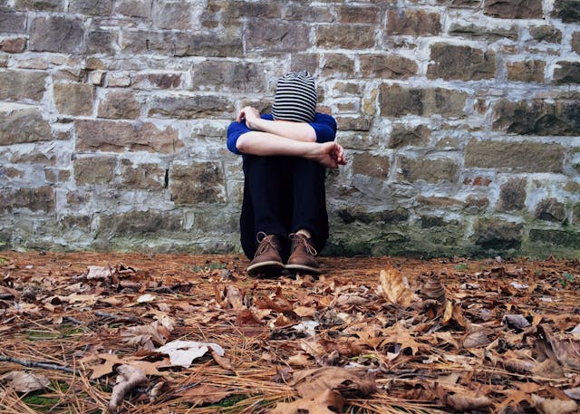 person sitting against the wall with arms crossed.