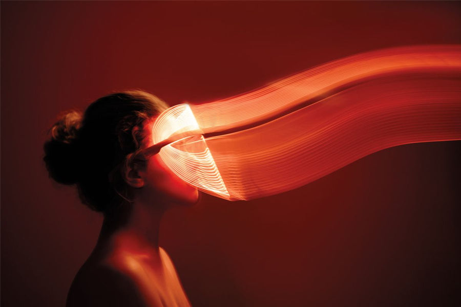Woman wearing a red light therapy face mask with glowing light effects against a dark background
