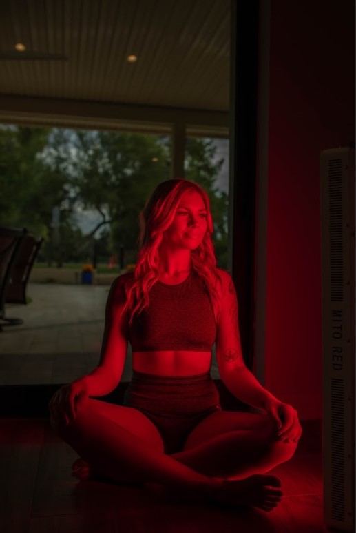 woman siting cross legged in front of red light therapy panel